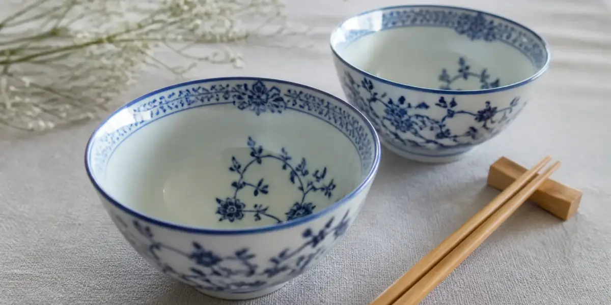 Deux bols en porcelaine bleu et blanc et des baguettes en bambou sur une nappe de lin, lumière du jour