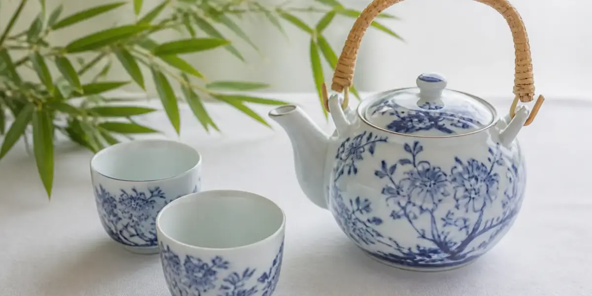 Théière en porcelaine bleu et blanc et deux tasses sans anse sur une nappe blanche