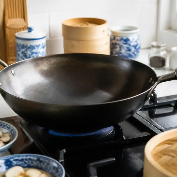 Wok en acier noir posé sur un feu de gaz, intérieur patiné, sur un plan de travail clair