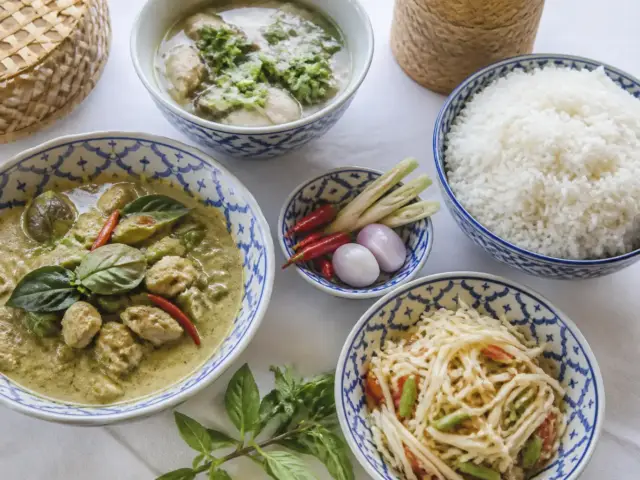 Plusieurs plats thaïlandais partagés autour d’un grand bol de riz, avec herbes fraîches et piments