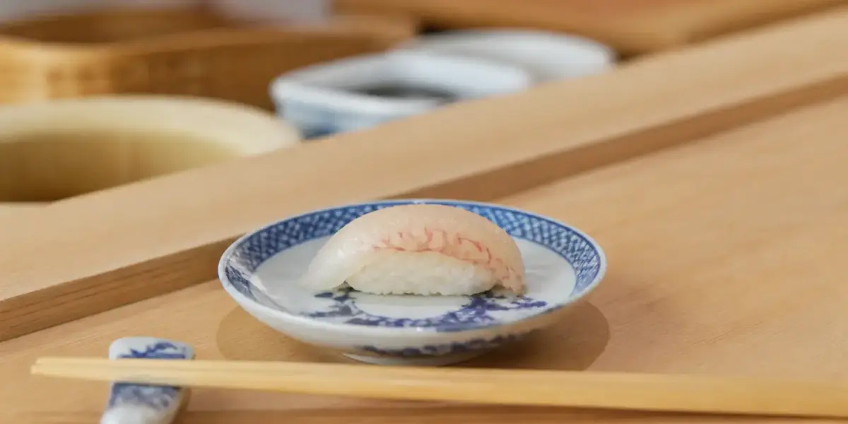 Pièce de sushi posée sur un comptoir en bois clair devant une assiette en porcelaine bleu et blanc