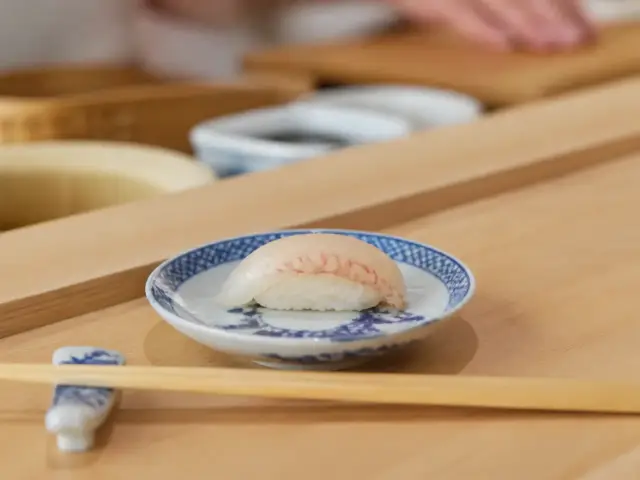 Pièce de sushi posée sur un comptoir en bois clair devant une assiette en porcelaine bleu et blanc