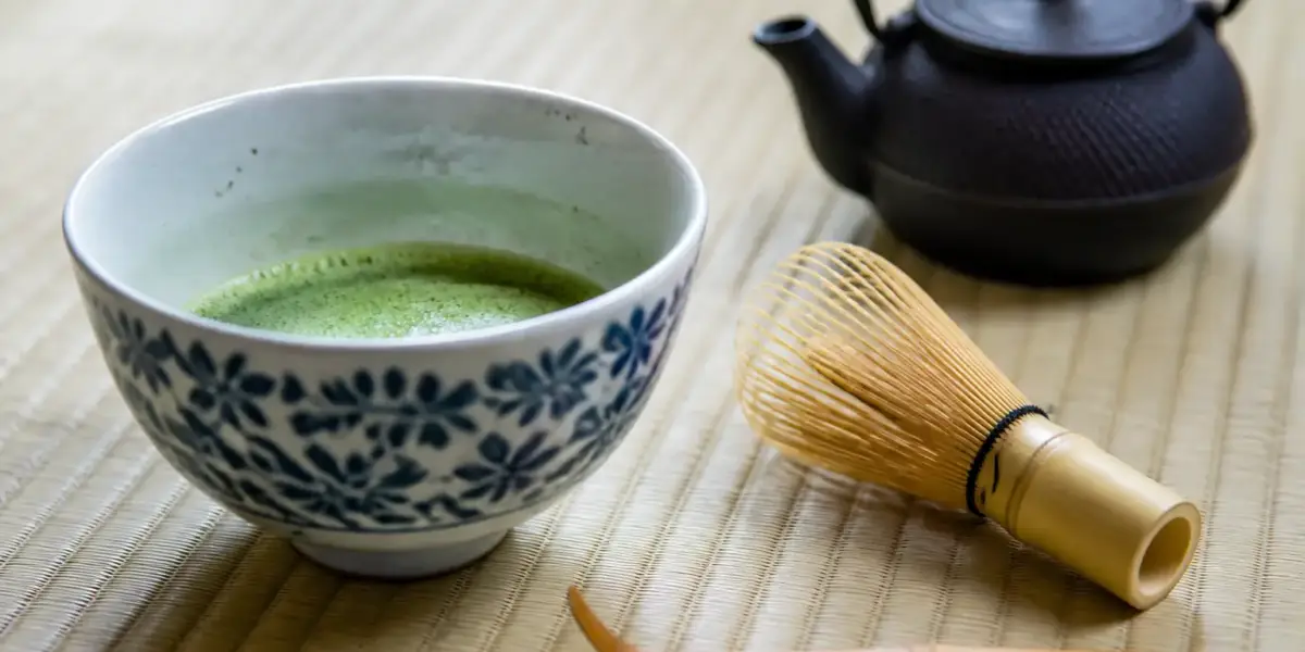 Bol de thé matcha mousseux, fouet en bambou et cuillère posés sur un tatami dans une salle de thé