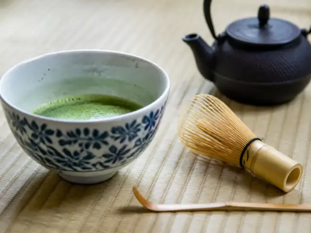 Bol de thé matcha mousseux, fouet en bambou et cuillère posés sur un tatami dans une salle de thé