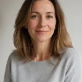 Portrait d’Hélène Marchadier, cheveux châtain clair mi-longs, pull gris perle, fond de pièce claire et floue