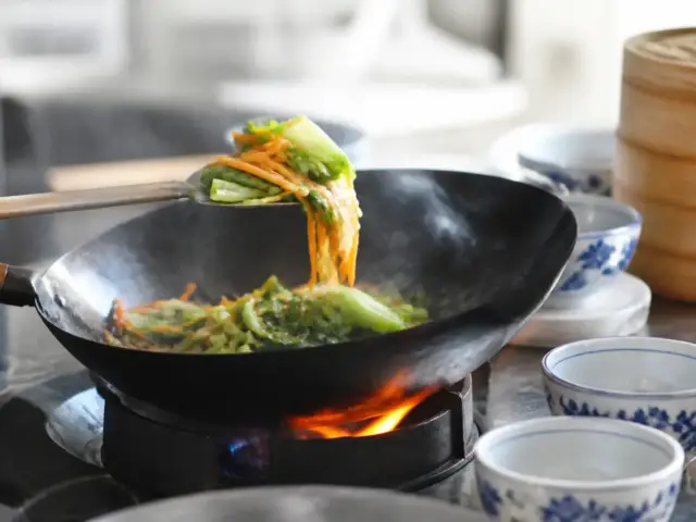 Légumes coupés en lamelles qui sautent dans un wok noir au-dessus d’une flamme vive, spatule en métal