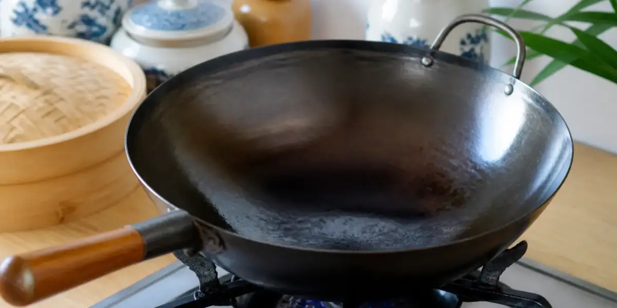 Wok en acier noirci posé sur une flamme, sa paroi intérieure luisante d’une fine couche d’huile