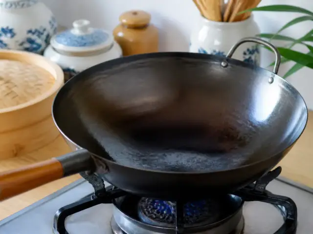 Wok en acier noirci posé sur une flamme, sa paroi intérieure luisante d’une fine couche d’huile