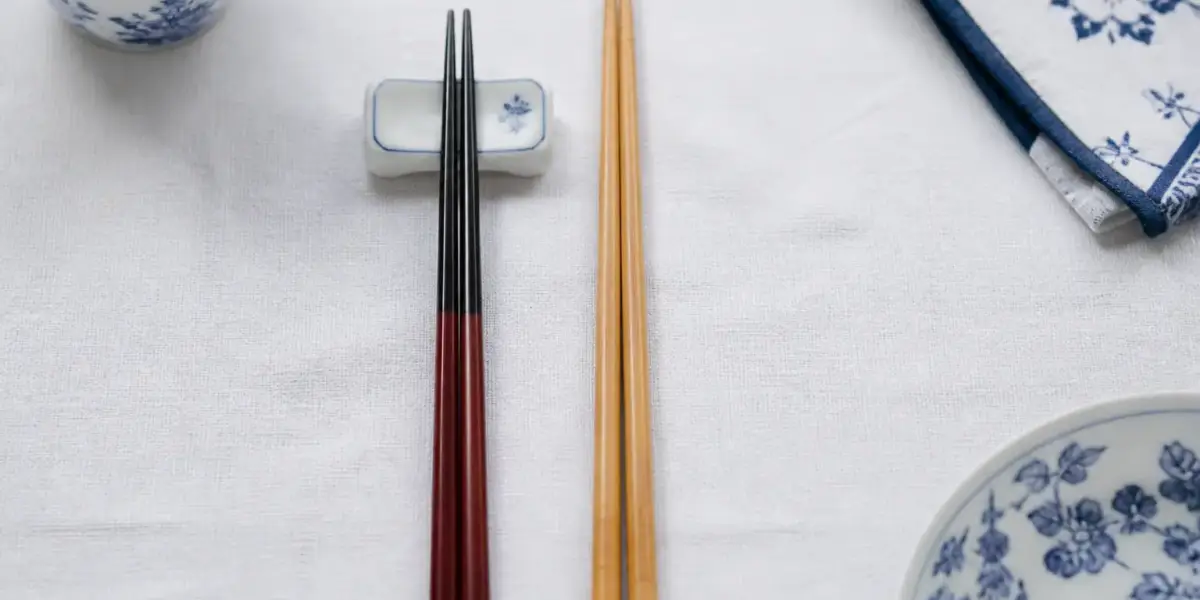 Deux paires de baguettes posées côte à côte, une japonaise laquée à pointe fine et une chinoise plus longue en bambou