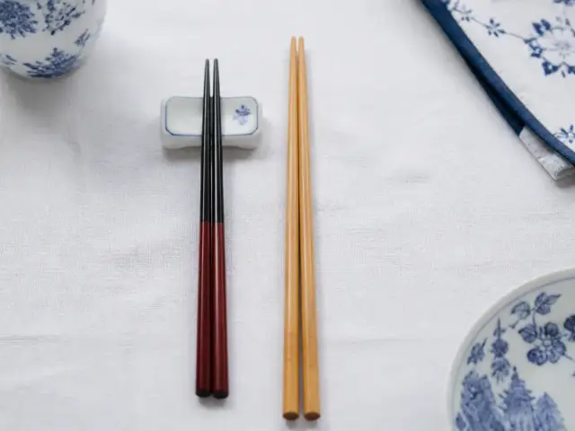 Deux paires de baguettes posées côte à côte, une japonaise laquée à pointe fine et une chinoise plus longue en bambou