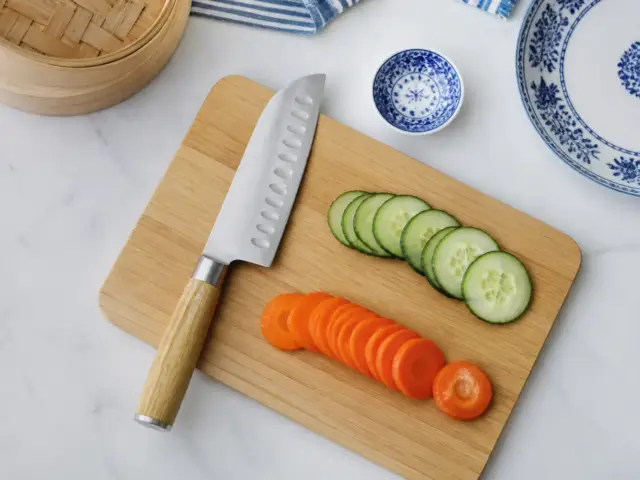 Couteau santoku à lame alvéolée posé sur une planche en bois à côté de légumes émincés