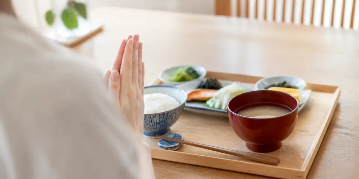 Mains jointes devant un plateau de repas japonais avec bol de riz, bol de soupe laqué et baguettes posées