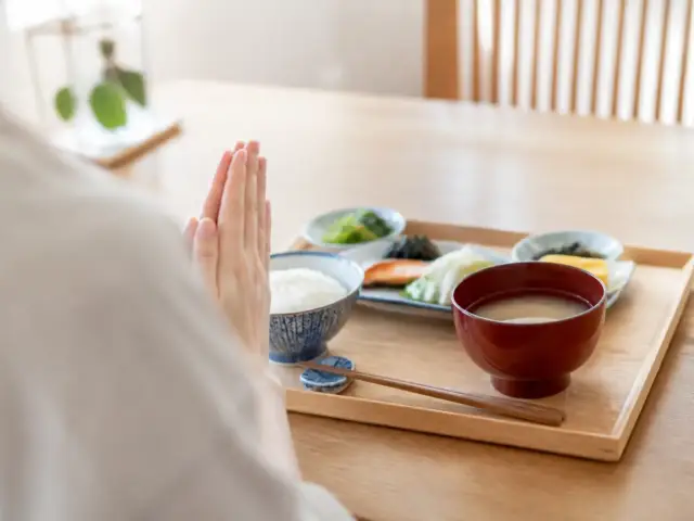 Mains jointes devant un plateau de repas japonais avec bol de riz, bol de soupe laqué et baguettes posées