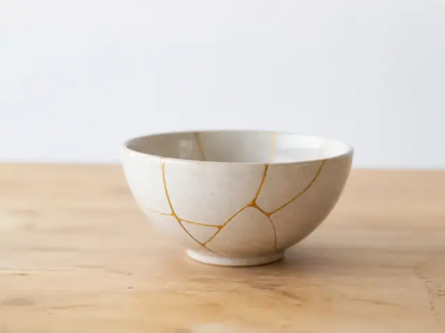 Bol en céramique beige réparé au kintsugi, ses fissures recouvertes de fines lignes dorées