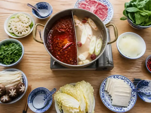 Marmite de hot pot à deux compartiments, bouillon rouge et bouillon clair, posée sur un réchaud au centre d’une table