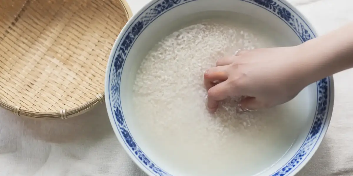 Mains qui remuent du riz blanc dans un grand bol d’eau trouble au-dessus d’un évier
