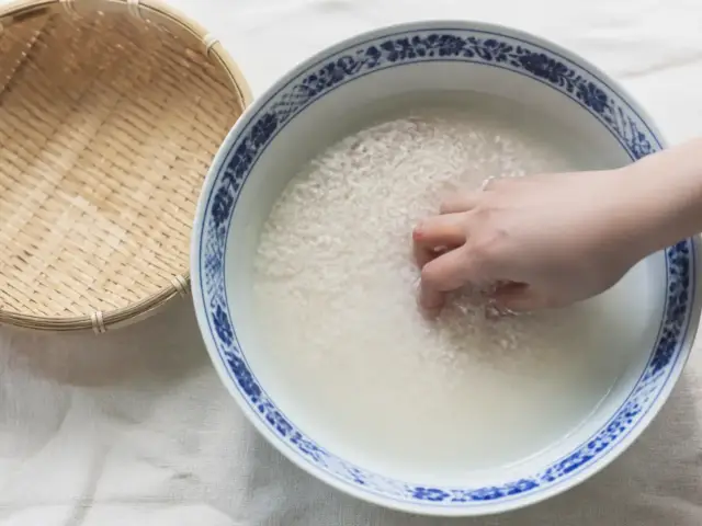 Mains qui remuent du riz blanc dans un grand bol d’eau trouble au-dessus d’un évier